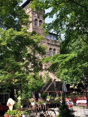 Biergarten im Schatten von Bäumen im Hintergrund ein Steinerner Aussichtsturm